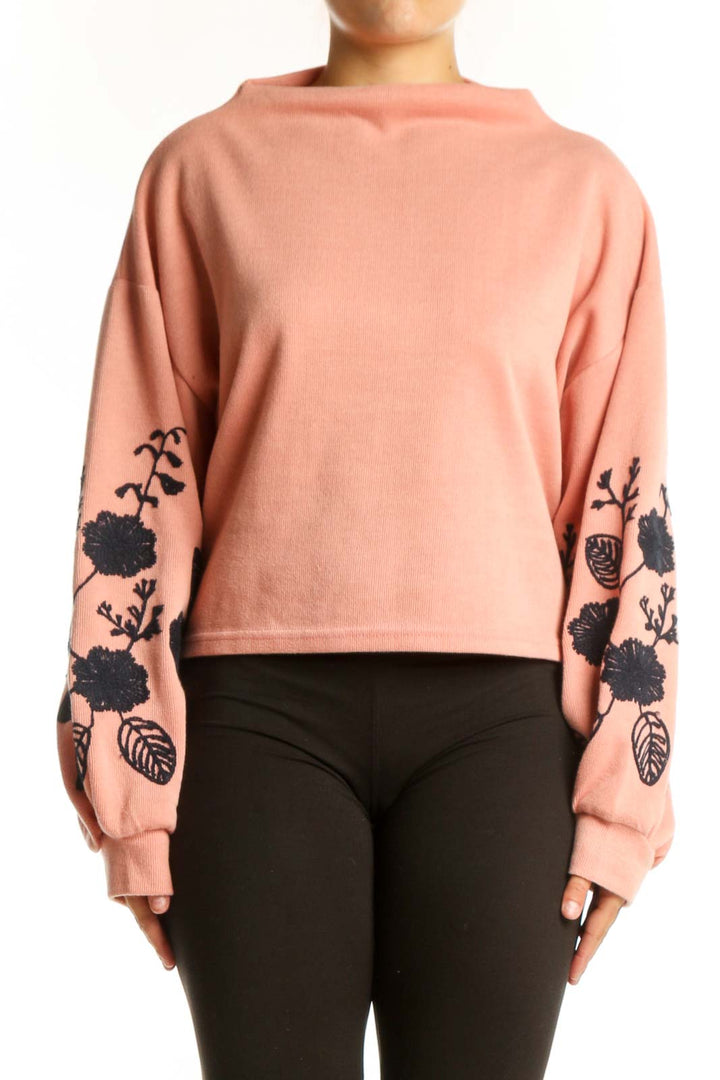 Peach cropped sweatshirt with black floral embroidery on sleeves, front view