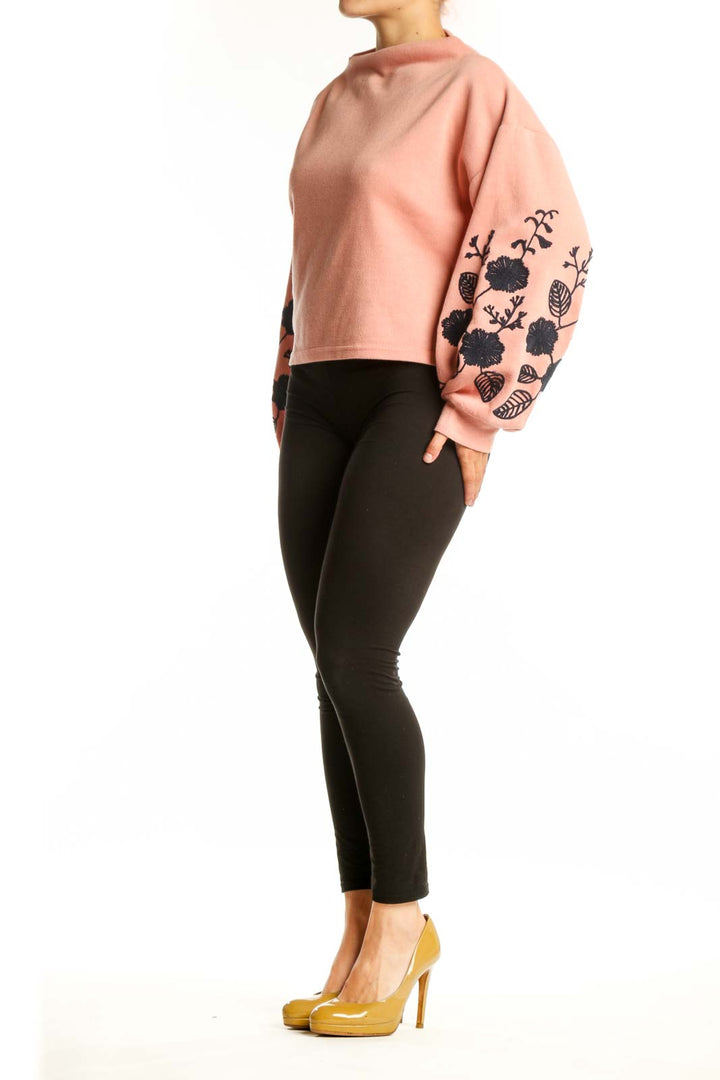 Peach cropped sweatshirt with black floral embroidery on sleeves, front view