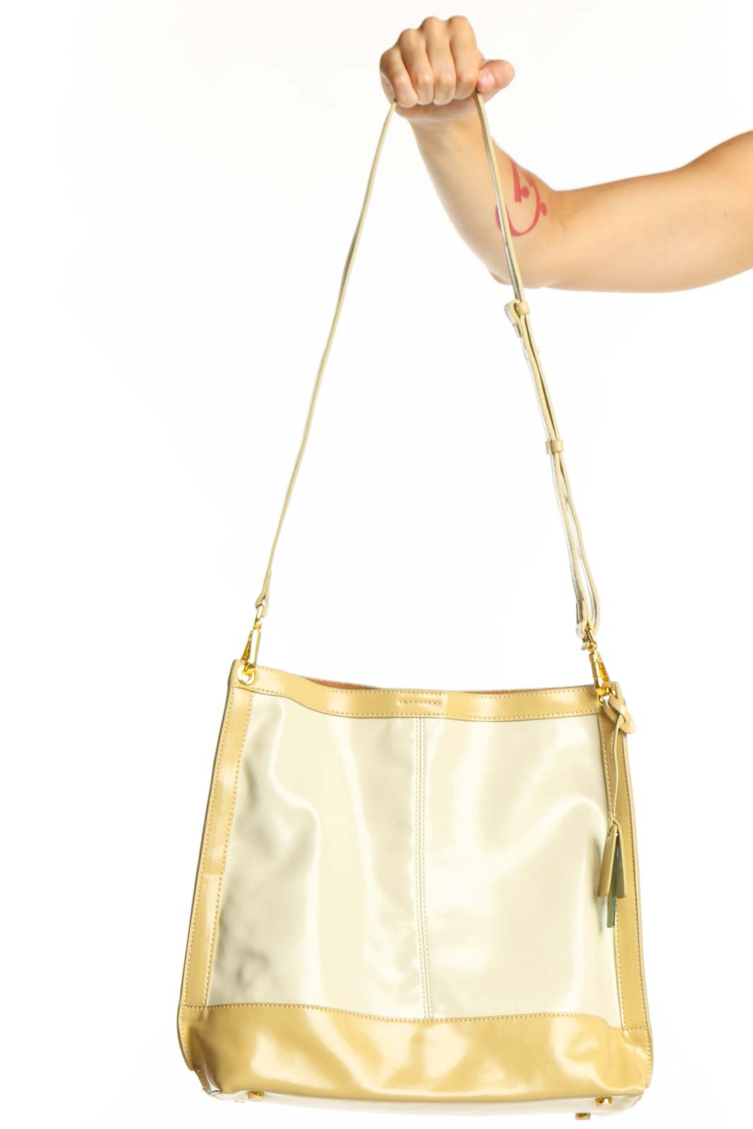 SilkRoll gold and cream leather crossbody bag with adjustable strap held in hand, showing front view with color-block design
