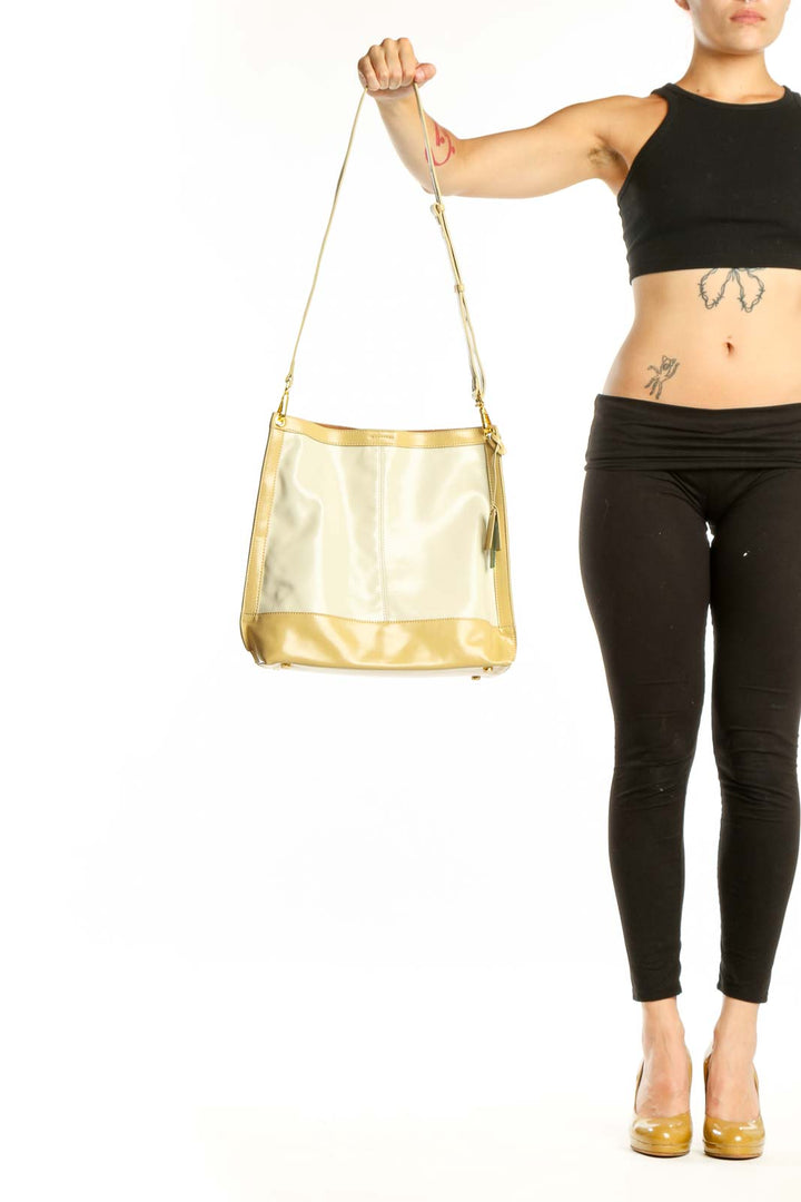 SilkRoll gold and cream leather crossbody bag with adjustable strap held in hand, showing front view with color-block design