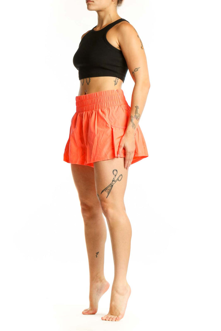 Woman wearing orange ruched high-waisted athletic shorts with black sports bra, front view