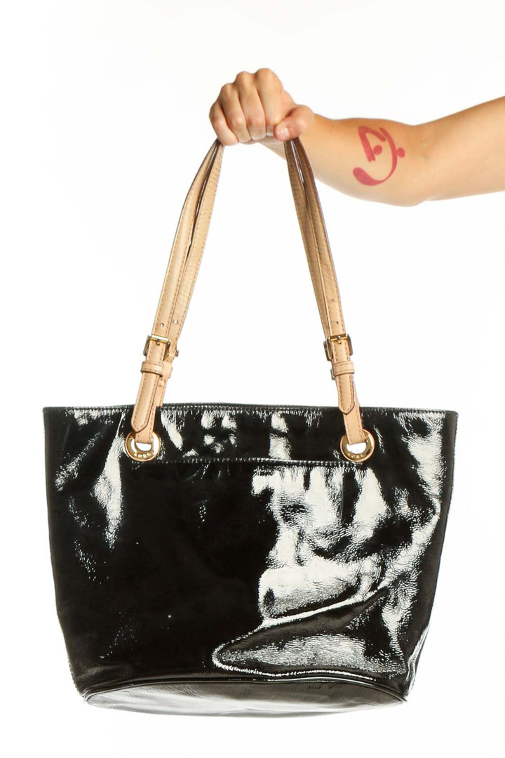 Black patent leather Michael Kors tote bag with tan handles held by model, front view