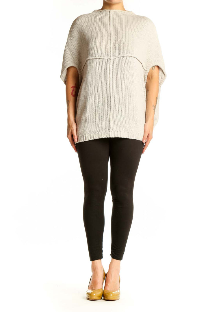 Cream acrylic knit poncho with cutout sleeves, back view showing ribbed texture and oversized fit