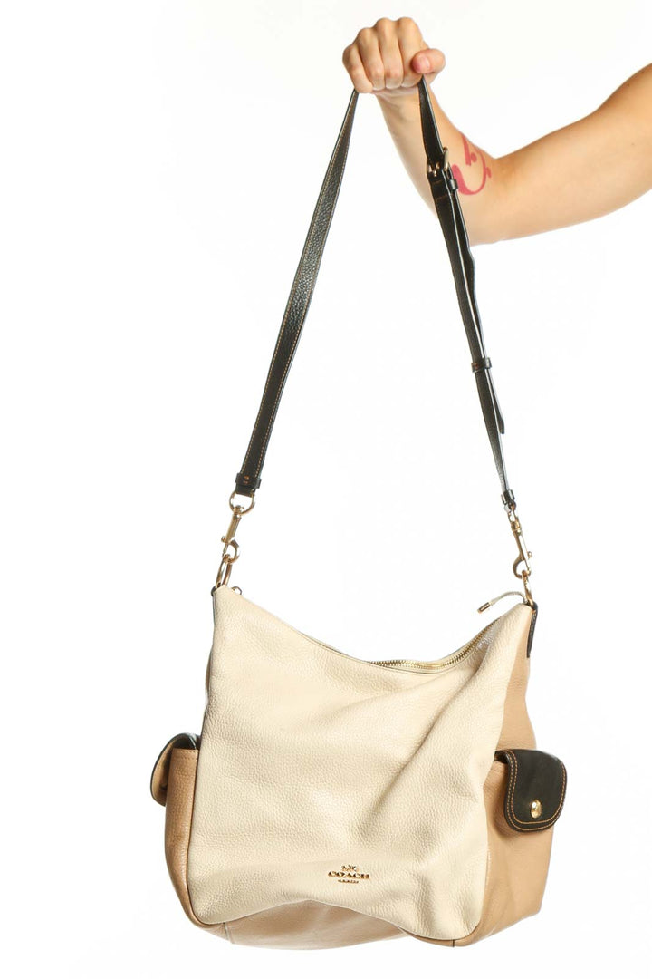 Cream and tan Coach leather crossbody bag with black adjustable strap held by model