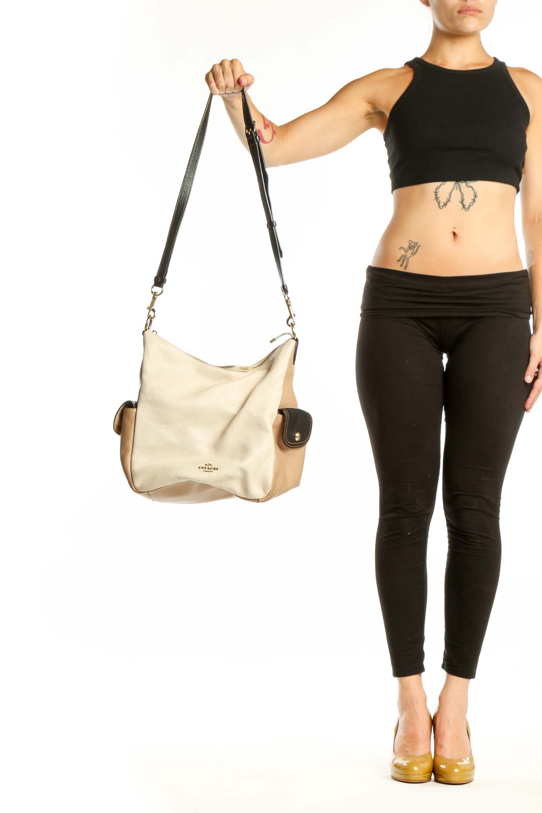 Cream and tan Coach leather crossbody bag with black adjustable strap held by model