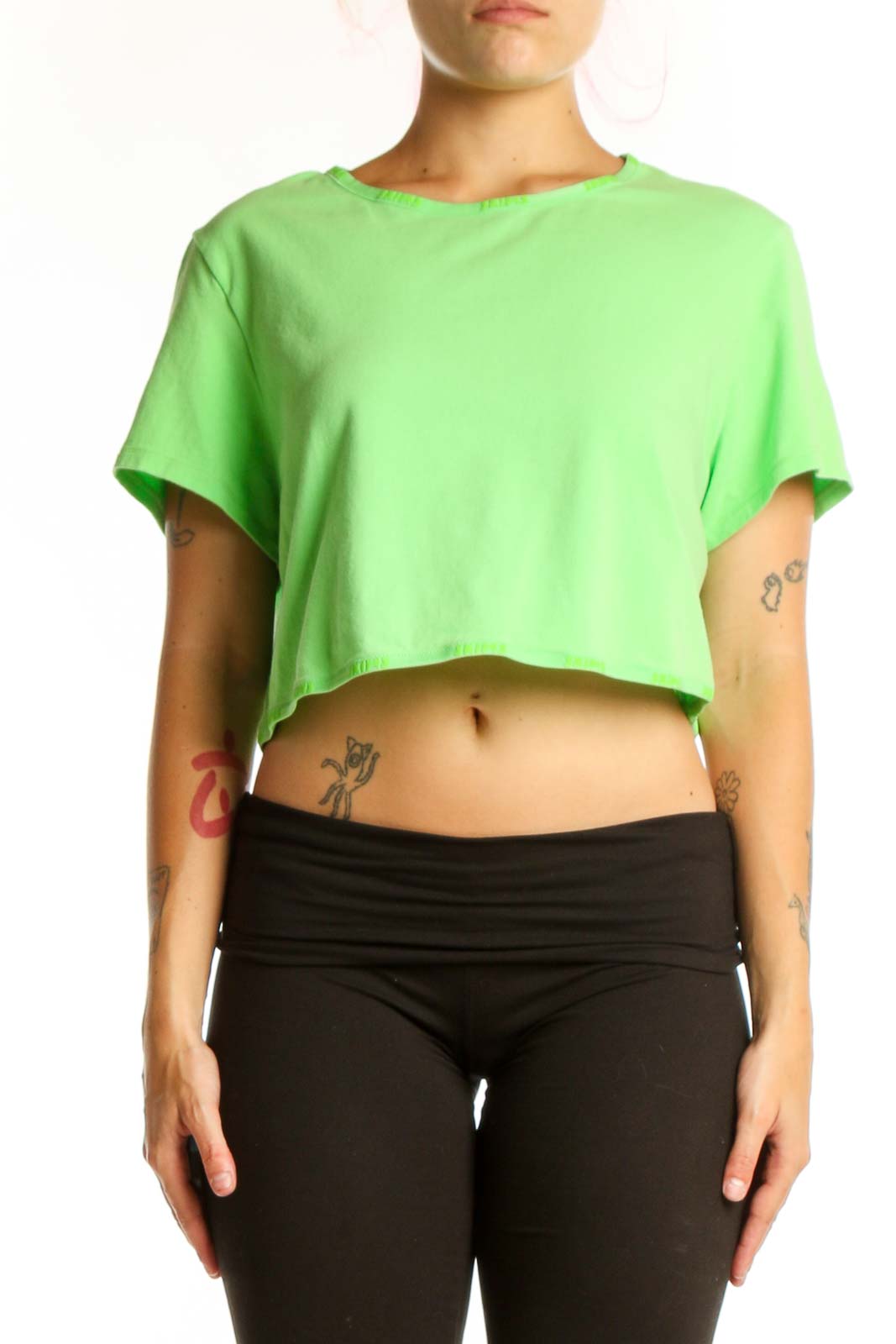 Woman wearing vibrant green cropped short sleeve t-shirt by Skims, paired with black leggings, front view