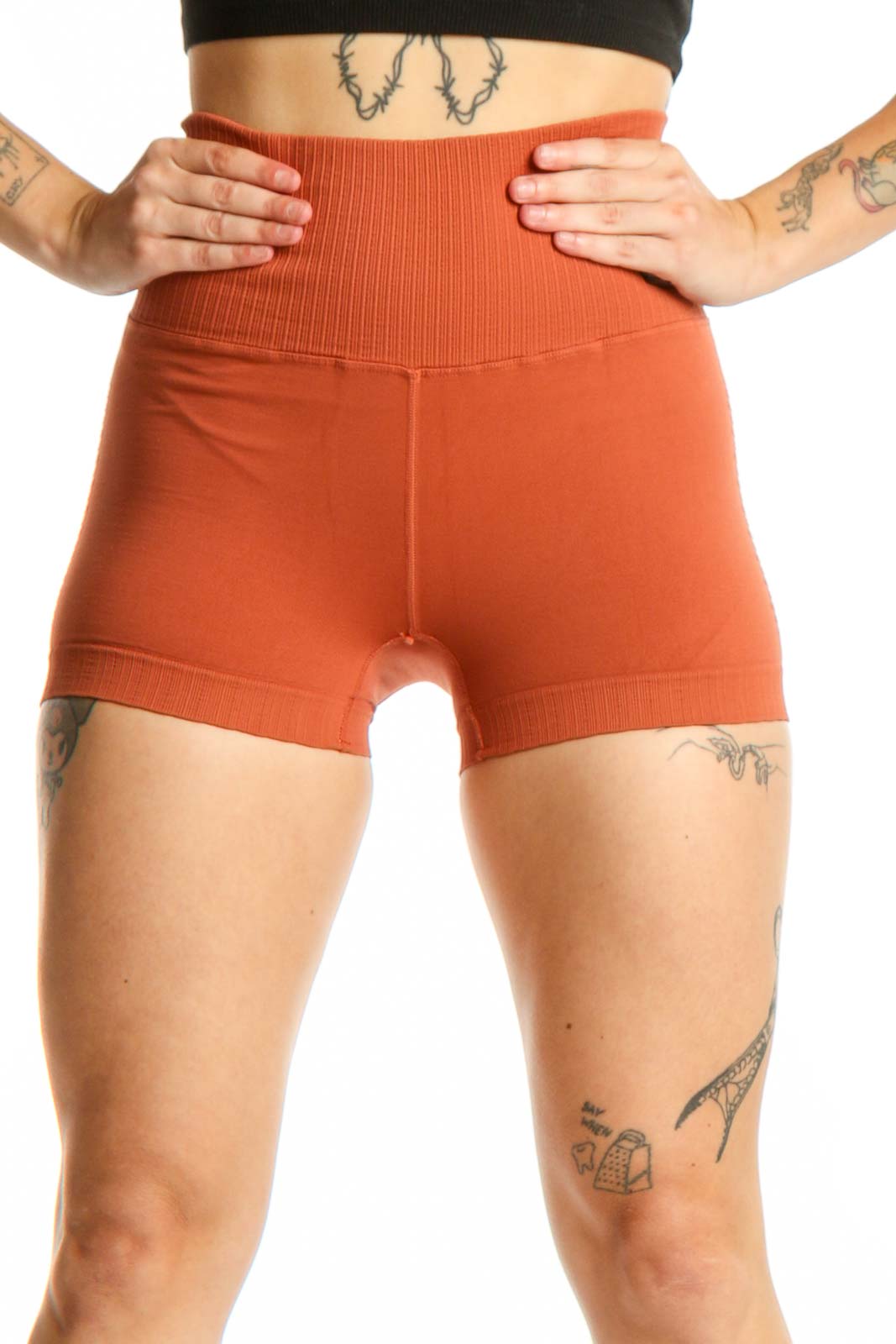 Woman wearing orange ribbed high-waist activewear shorts with black sports bra, front view