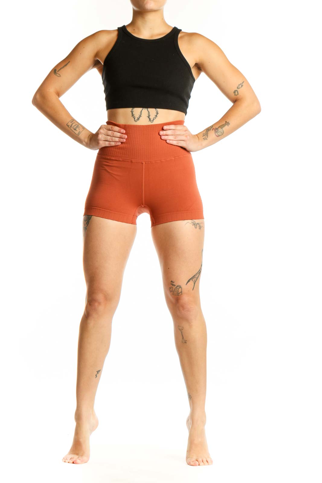 Woman wearing orange ribbed high-waist activewear shorts with black sports bra, front view