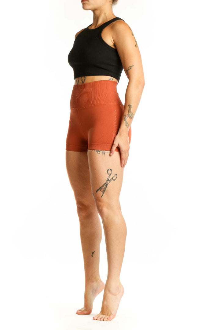 Woman wearing orange ribbed high-waist activewear shorts with black sports bra, front view