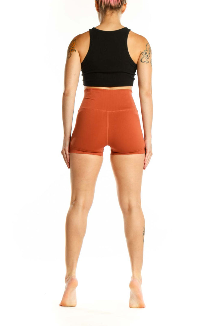 Woman wearing orange ribbed high-waist activewear shorts with black sports bra, side view showing fit
