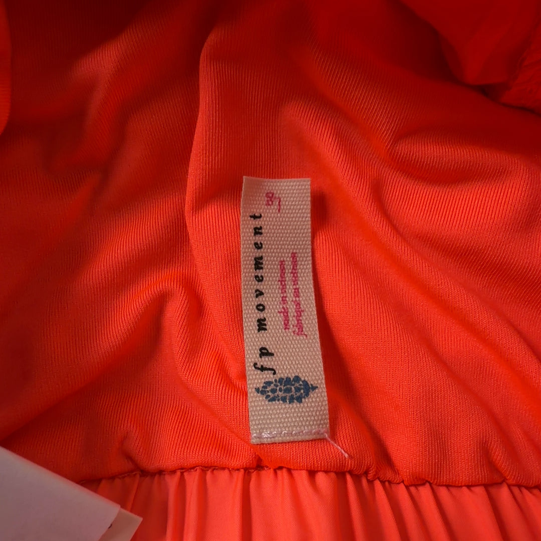 Woman wearing orange ruched athletic shorts with black sports bra, back view showing flared silhouette