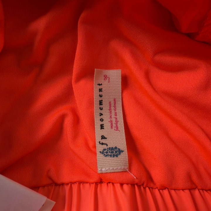 Woman wearing orange ruched athletic shorts with black sports bra, back view showing flared silhouette