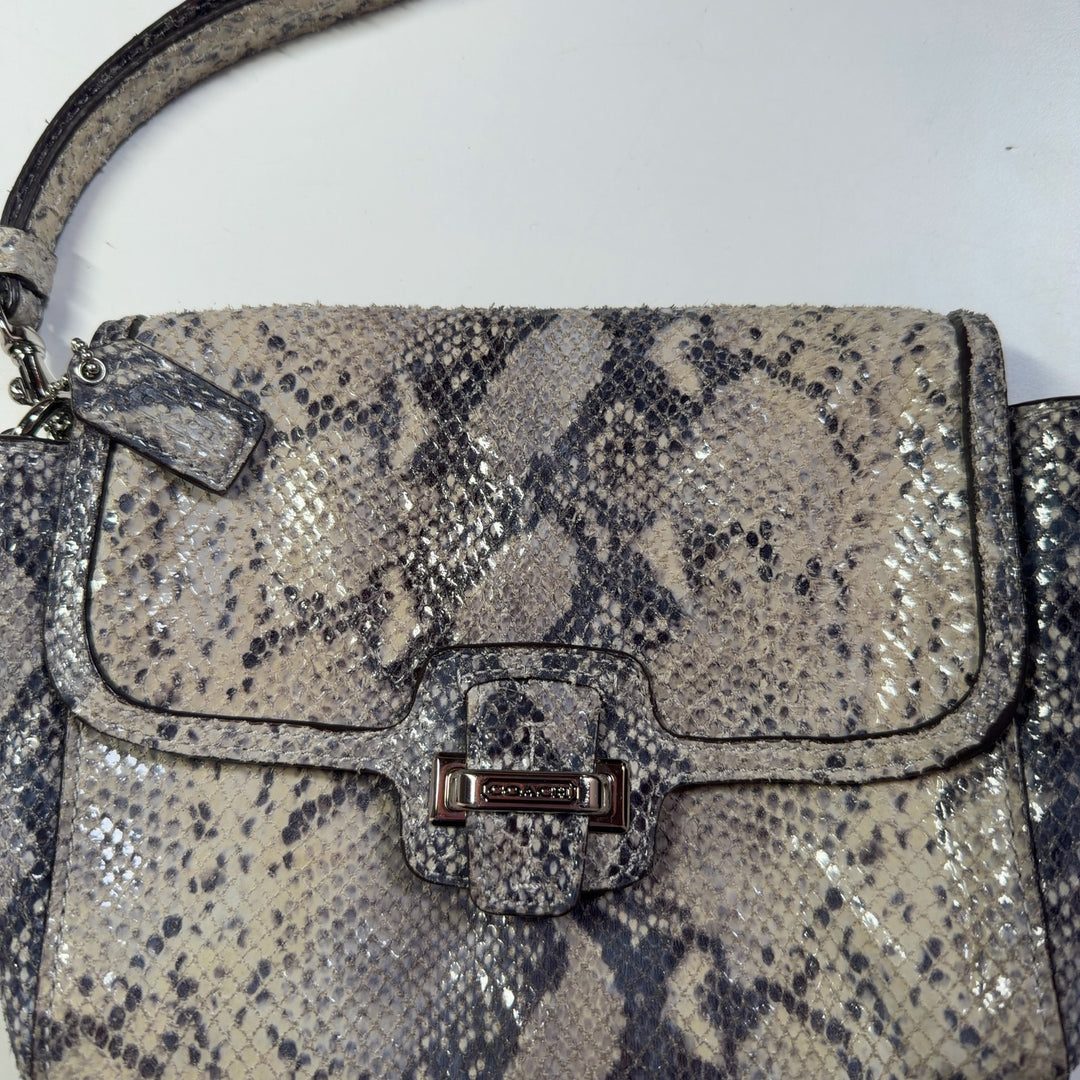 Tag view of beige python print Coach clutch wristlet being held, showing snakeskin texture and design details