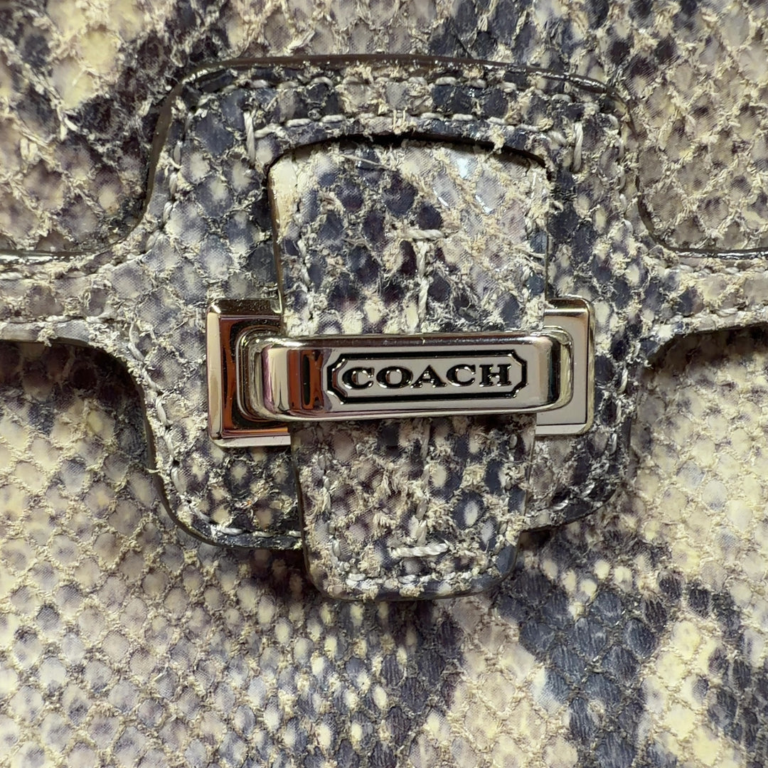 Tag view of beige python print Coach clutch wristlet being held, showing snakeskin texture and design details