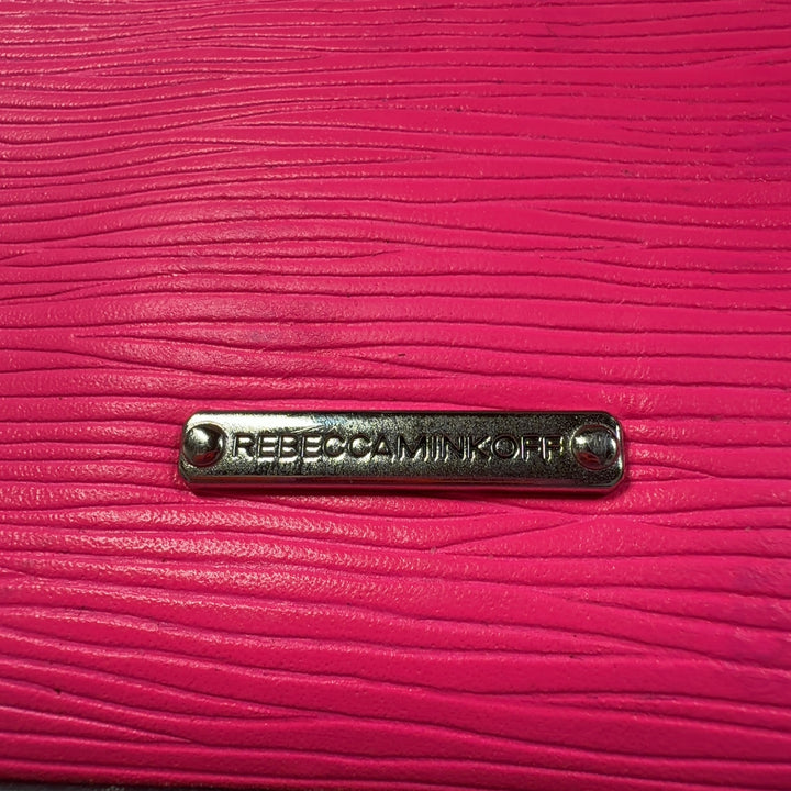 Tag view of pink Rebecca Minkoff crossbody bag worn on shoulder with adjustable chain strap