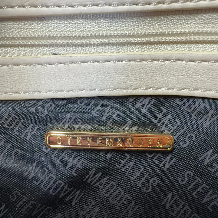 Tag view of cream quilted shoulder bag by Steve Madden with gold chain accent, worn on model's shoulder