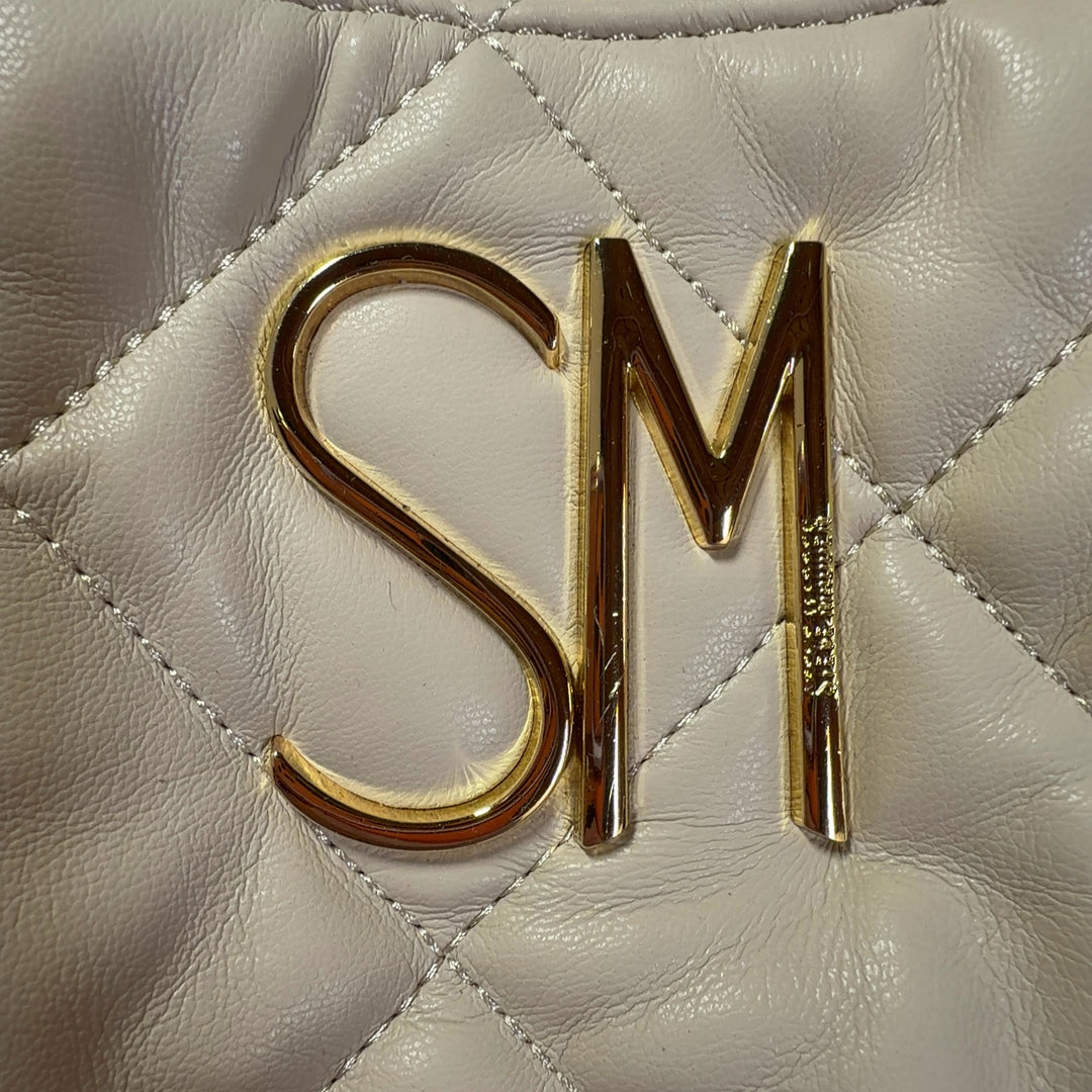 Tag view of cream quilted shoulder bag by Steve Madden with gold chain accent, worn on model's shoulder