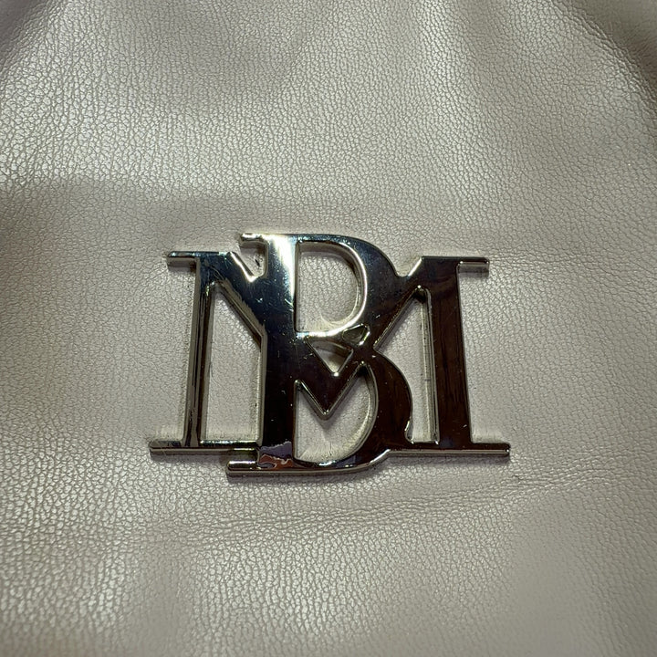 Tag view of cream Badgley Mischka shoulder bag worn on model's shoulder, displaying ruched texture and BM logo detail