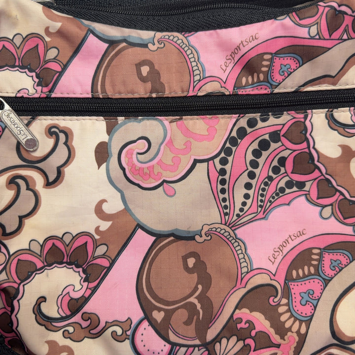 Pink paisley Lesportsac crossbody bag worn as crossbody style with black strap, back view on model