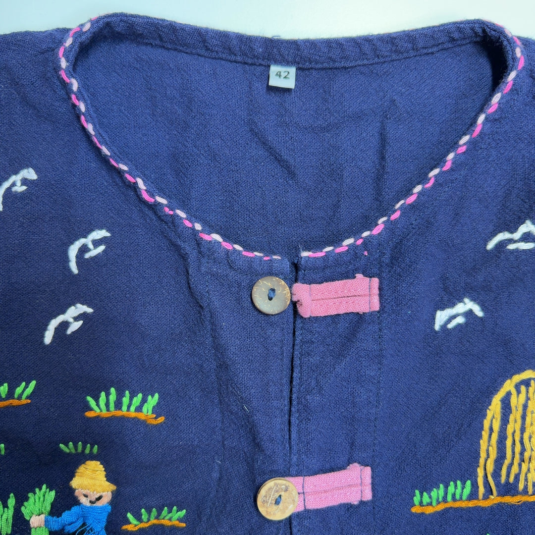 Tag view of navy embroidered SilkRoll top showing whimsical embroidered details and decorative stitching on patch pockets