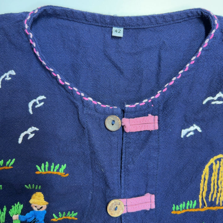 Tag view of navy embroidered SilkRoll top showing whimsical embroidered details and decorative stitching on patch pockets