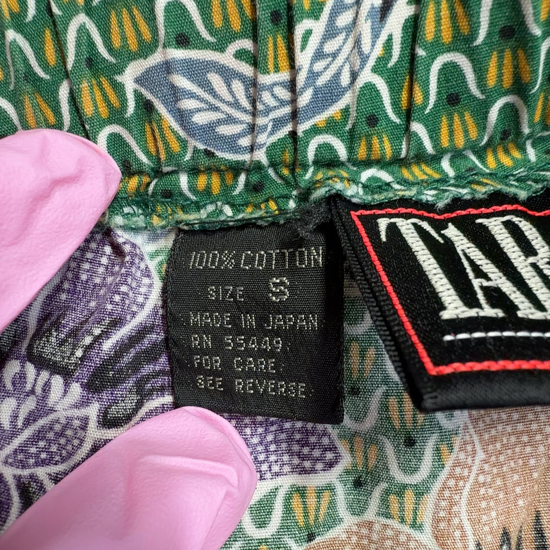 Tag view of green floral cropped pants showing the full botanical design and relaxed tapered silhouette