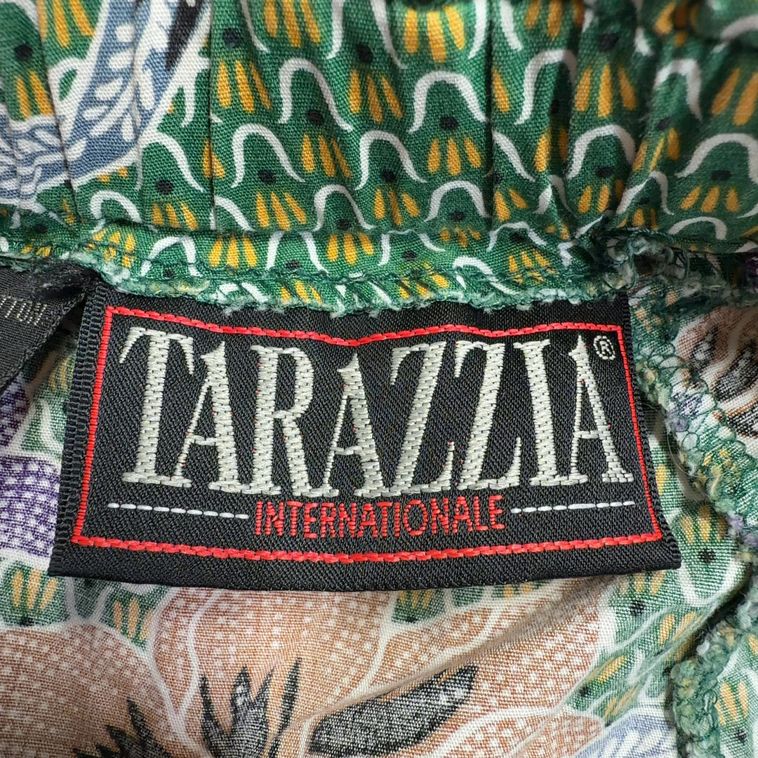 Tag view of green floral cropped pants showing the full botanical design and relaxed tapered silhouette