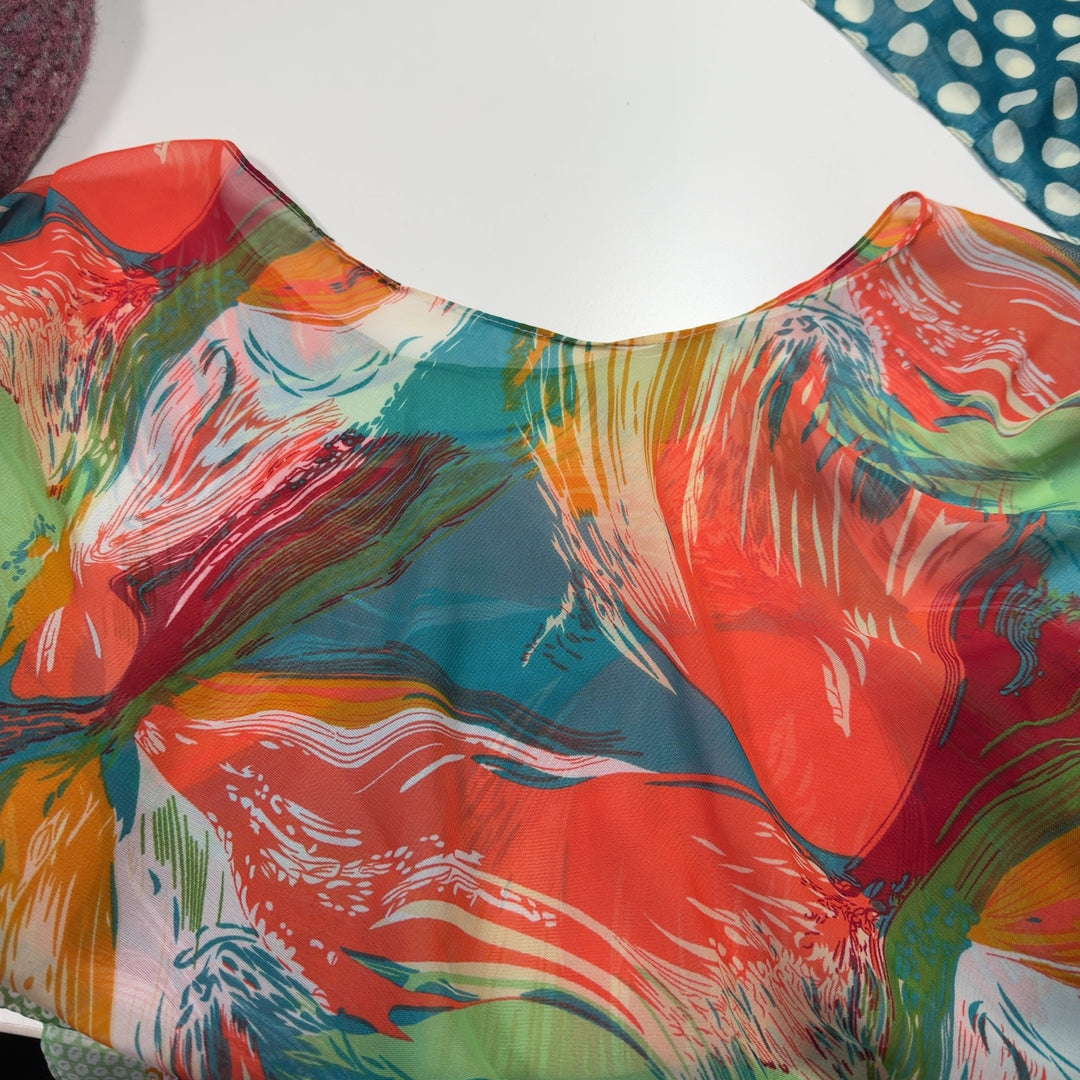 Tag view of multicolor poncho top showing artistic abstract print design and geometric dot and stripe details on lower section