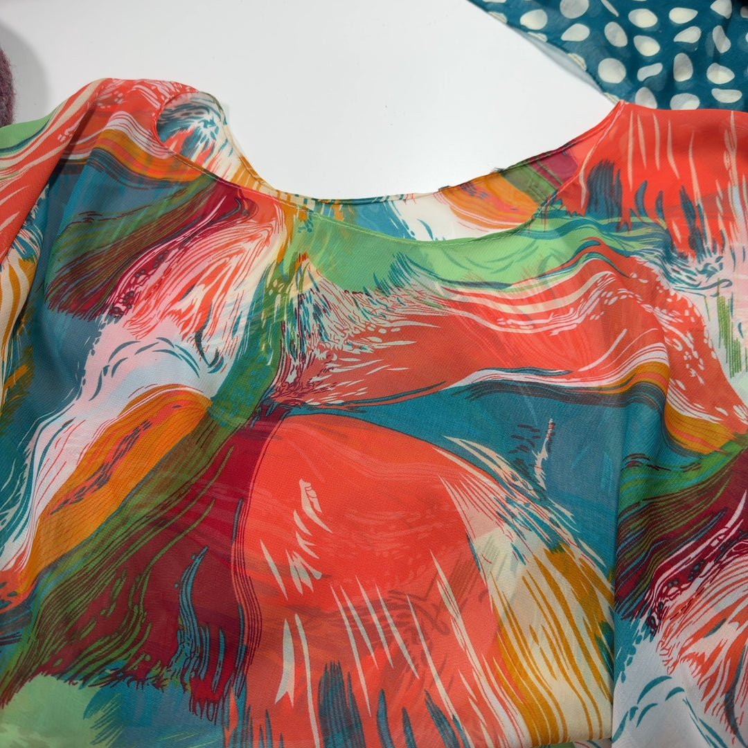 Tag view of multicolor poncho top showing artistic abstract print design and geometric dot and stripe details on lower section