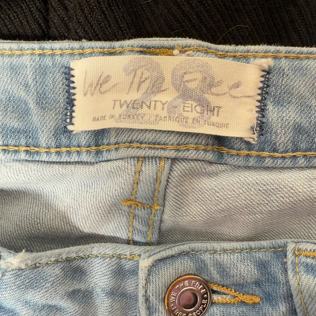Tag view of light blue denim flare jeans by WE THE FREE, size M, showing flare silhouette and five-pocket construction