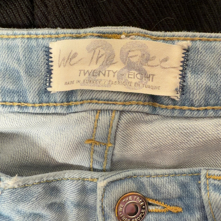 Tag view of light blue denim flare jeans by WE THE FREE, size M, showing flare silhouette and five-pocket construction