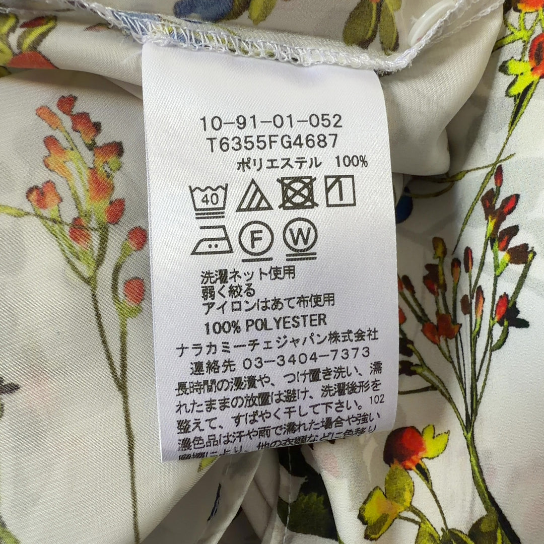 Tag view of cream floral blouse showing full botanical print pattern and tailored fit