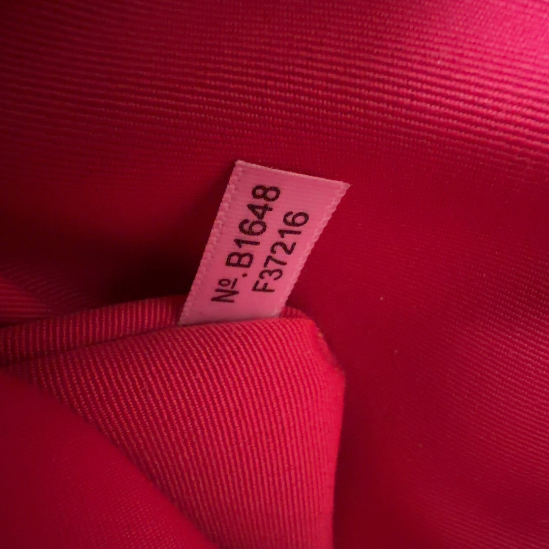 Tag view of pink Coach leather shoulder tote bag worn on woman's shoulder, showing structured silhouette and side pockets