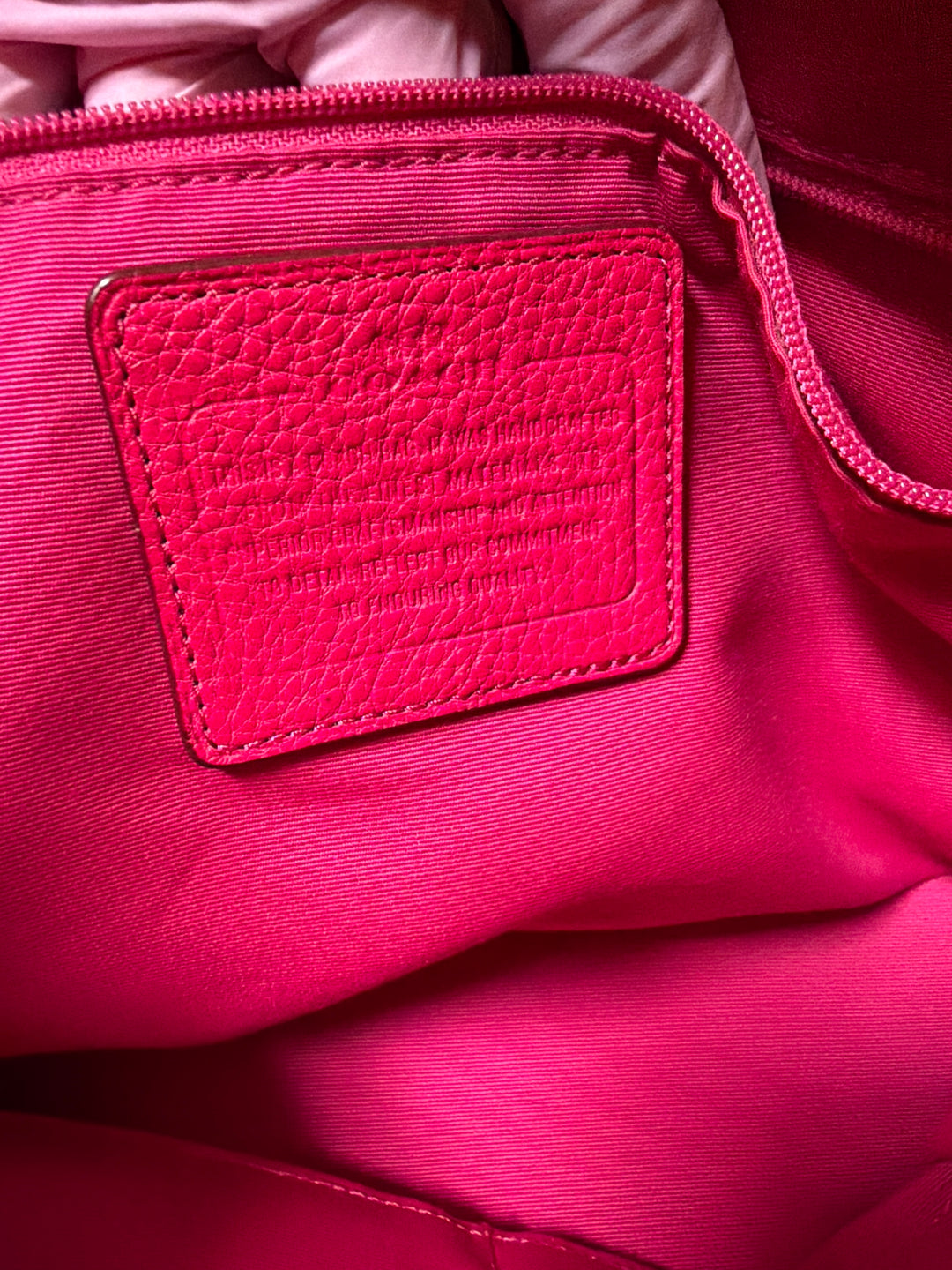 Tag view of pink Coach leather shoulder tote bag worn on woman's shoulder, showing structured silhouette and side pockets