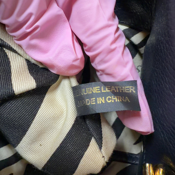 Tag view of black and gold striped leather tote bag worn on shoulder, showing horizontal stripe pattern and design details