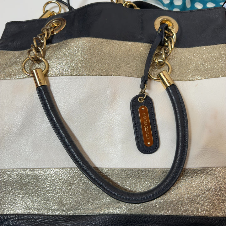Tag view of black and gold striped leather tote bag worn on shoulder, showing horizontal stripe pattern and design details