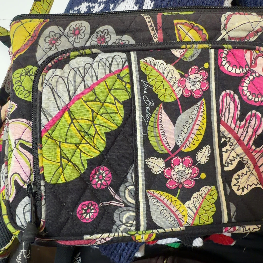 Tag view of black floral Vera Bradley crossbody bag worn as crossbody style with adjustable patterned strap