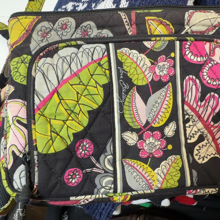 Tag view of black floral Vera Bradley crossbody bag worn as crossbody style with adjustable patterned strap