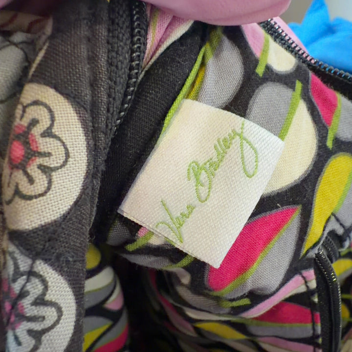 Tag view of black floral Vera Bradley crossbody bag worn as crossbody style with adjustable patterned strap