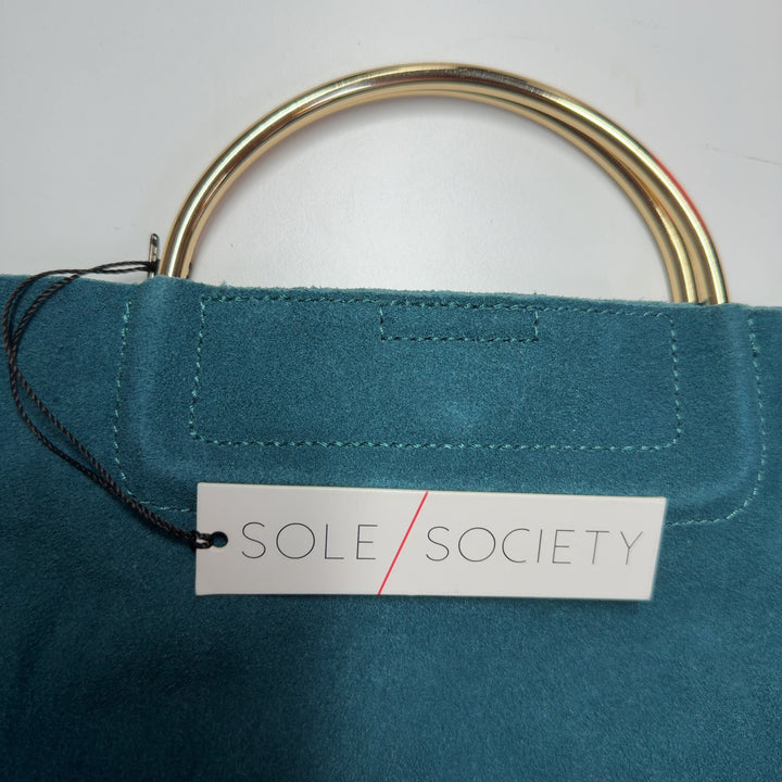Teal suede clutch with top handle displayed from side angle, worn with black outfit