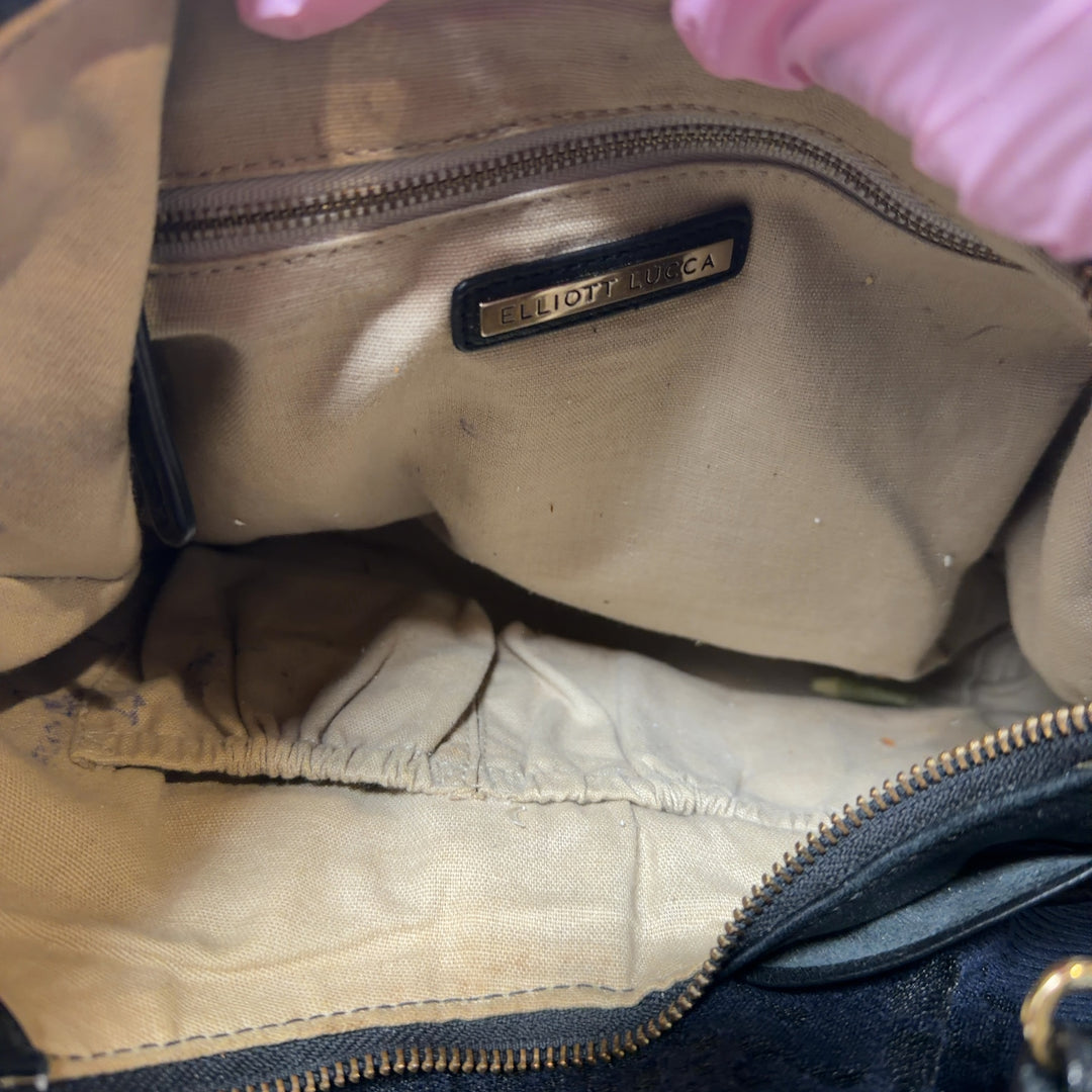 Tag view of black leather Elliott Lucca shoulder bag worn on shoulder, showing textured leather and bow design