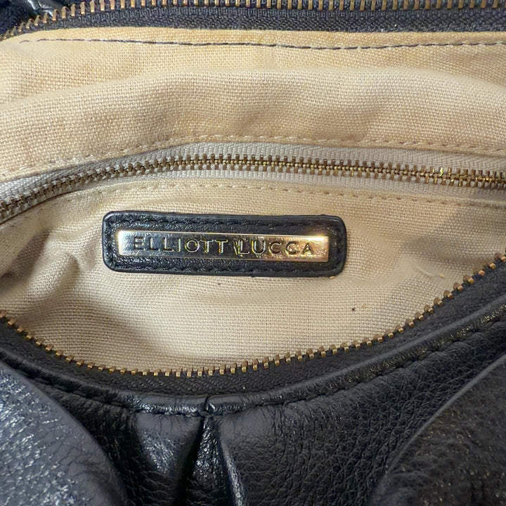 Tag view of black leather Elliott Lucca shoulder bag worn on shoulder, showing textured leather and bow design