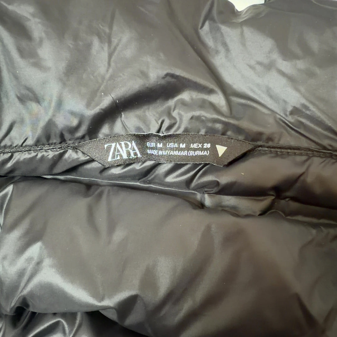 Tag view of black cropped puffer jacket showing quilted puffer design and knit sleeve details