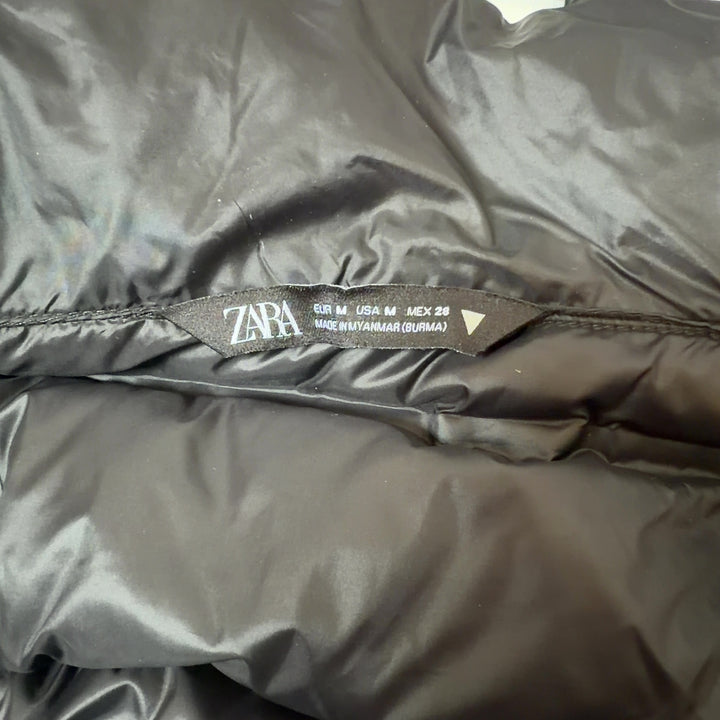 Tag view of black cropped puffer jacket showing quilted puffer design and knit sleeve details