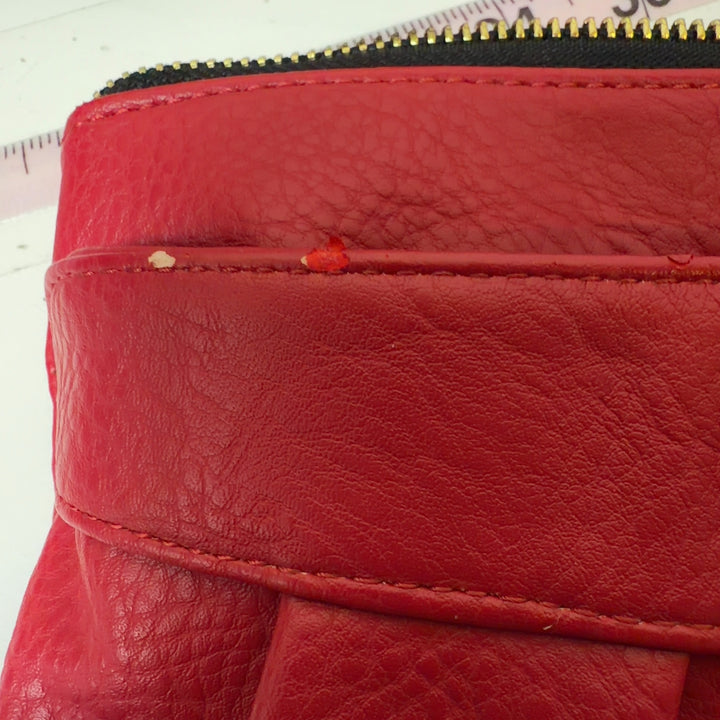 Red leather pleated clutch wristlet styled with black outfit, showing side profile and wristlet strap
