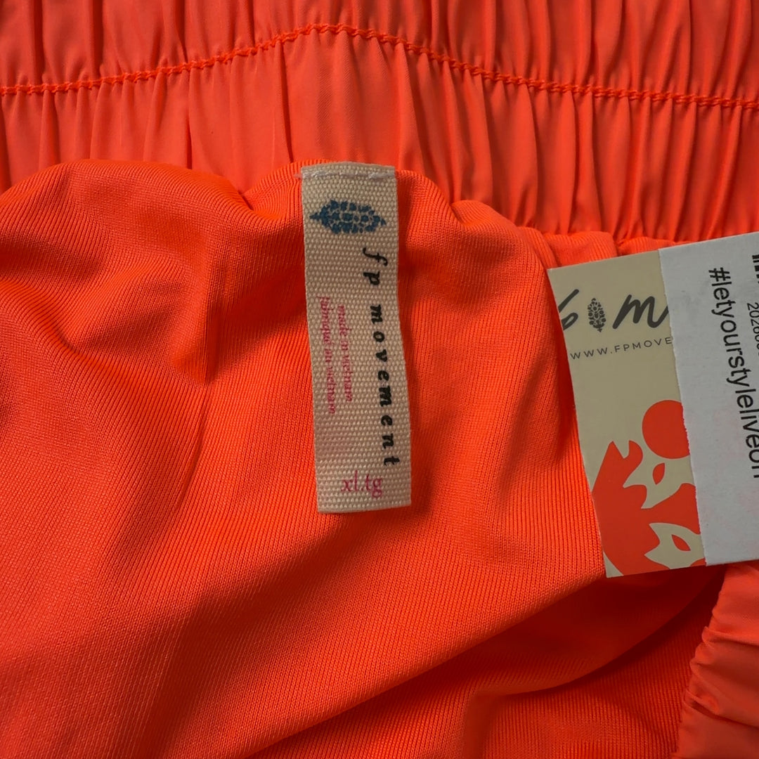 Tag view of coral pleated athletic skirt on model wearing black sports bra, displaying the flowing design and comfortable fit