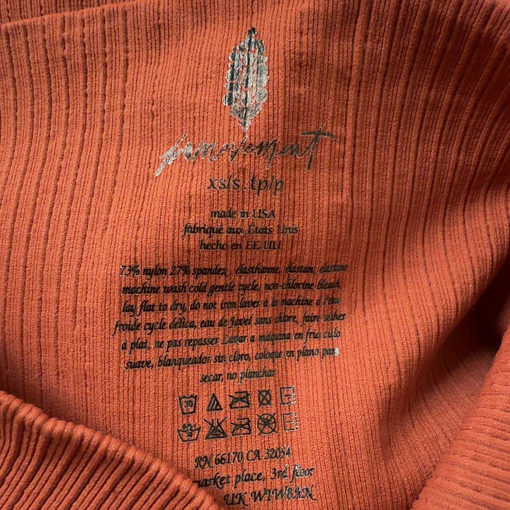 Woman wearing orange ribbed high-waist activewear shorts with black sports bra, side view showing fit