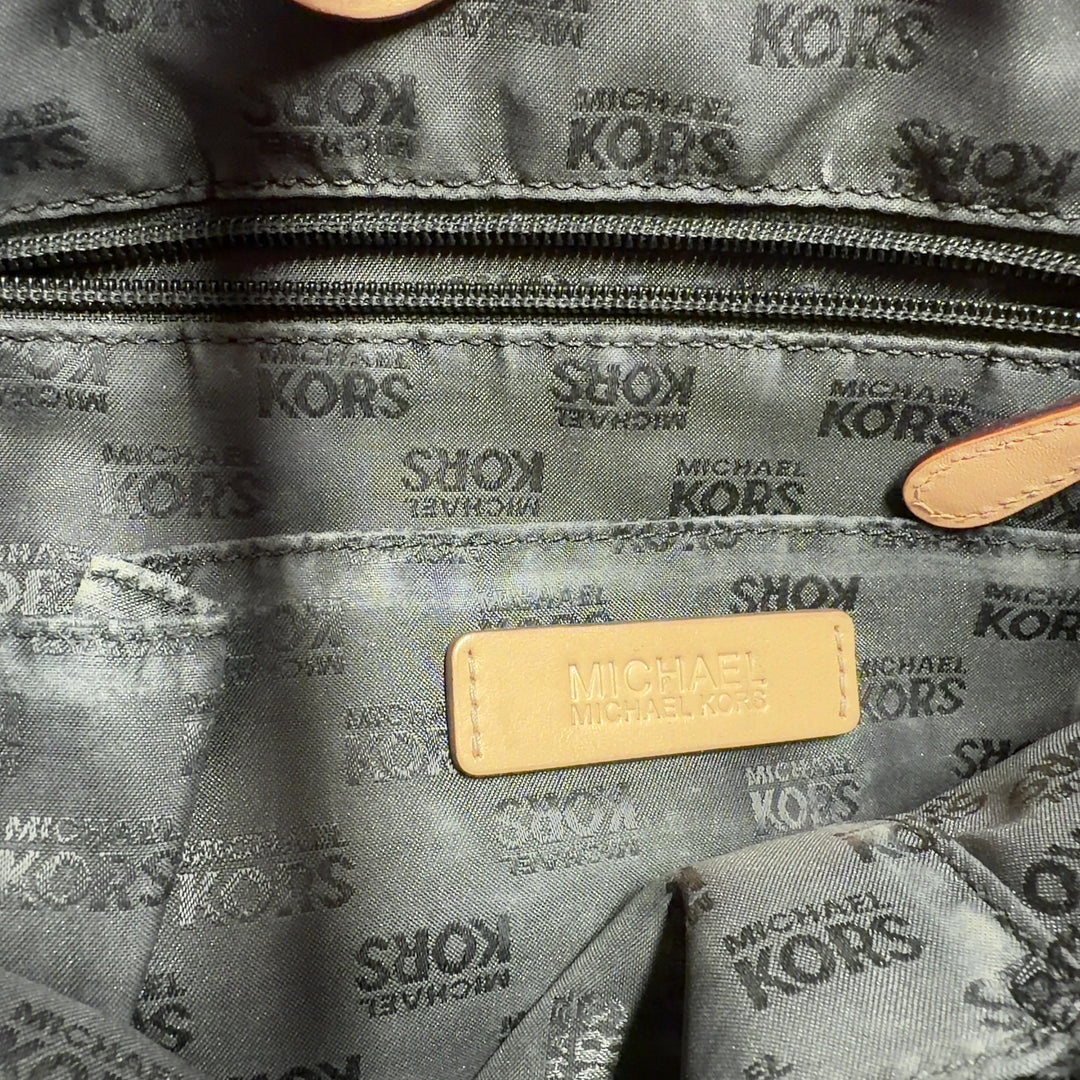 Black patent leather Michael Kors tote bag with tan handles worn on model's shoulder, back view