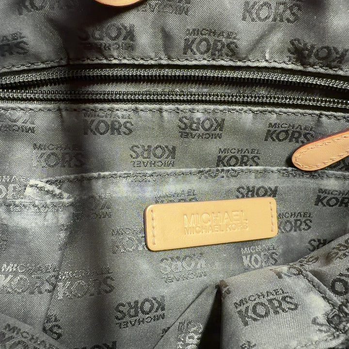 Black patent leather Michael Kors tote bag with tan handles worn on model's shoulder, back view