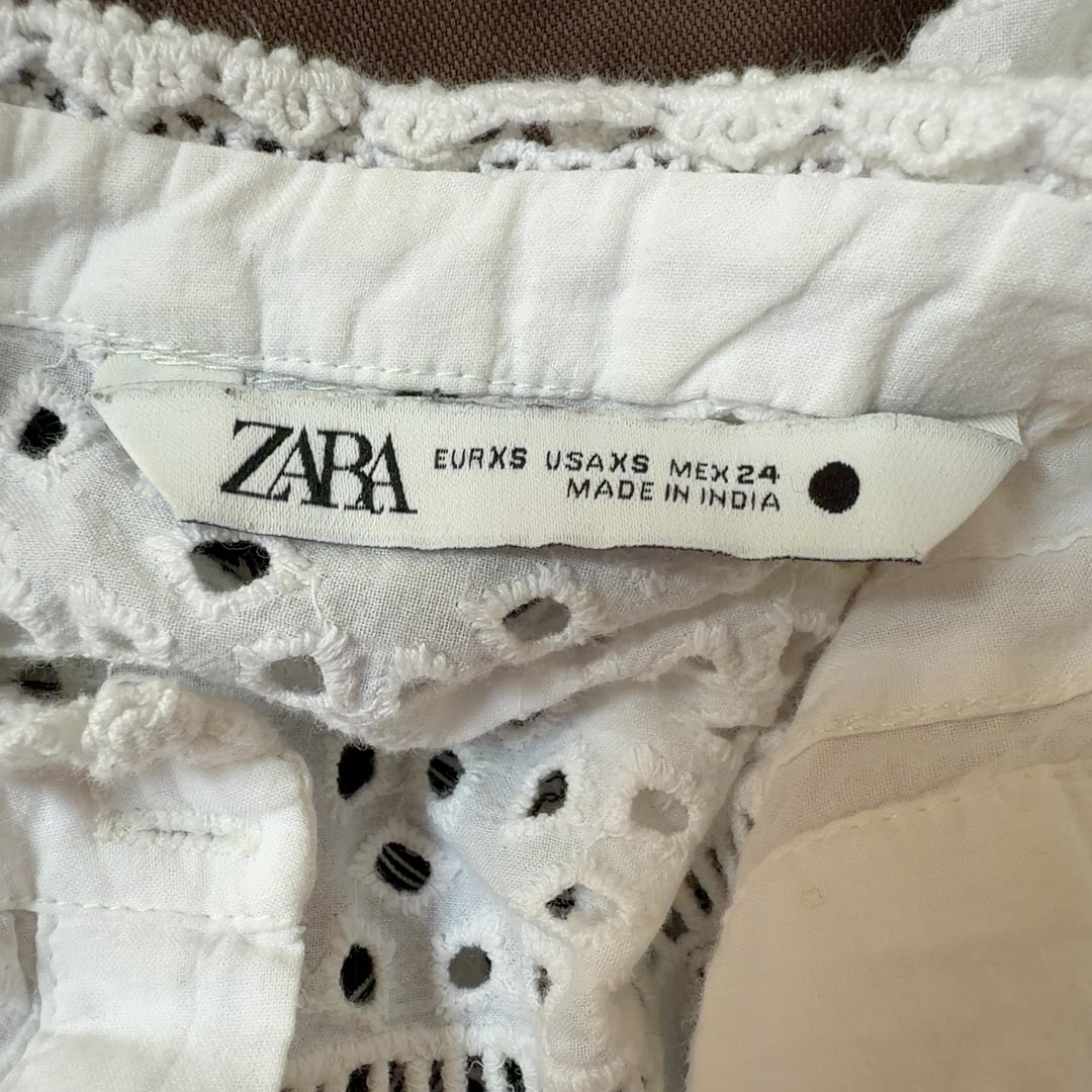 Tag view of cream eyelet cropped top showing lace pattern and pleated design